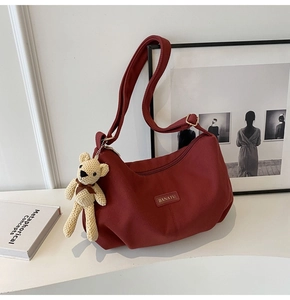 Detailed shot of dark red corduroy crossbody bag with cute beige knit bear charm