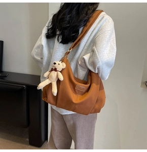 Detail of brown nylon crossbody bag with small bear pendant and brand logo patch