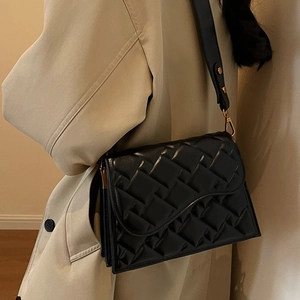 Elegante borsa a tracolla trapuntata nera con dettagli dorati su un cappotto beige classico