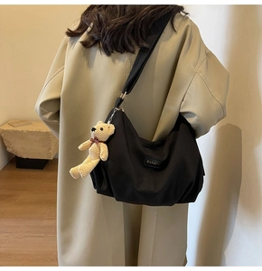 Detail of black nylon dumpling bag featuring a woven logo and cute bear pendant accessory