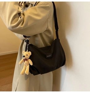 Detail of black nylon dumpling bag featuring adjustable strap and yellow bear charm accent