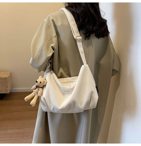 Detailed texture of white corduroy dumpling bag with branded patch and bear charm