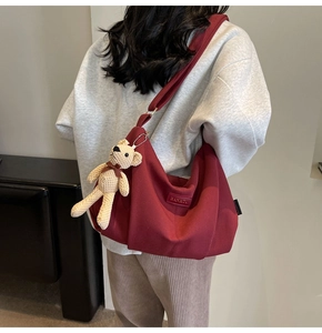 Detail view of large burgundy nylon bag with beige bear pendant and leather logo tag