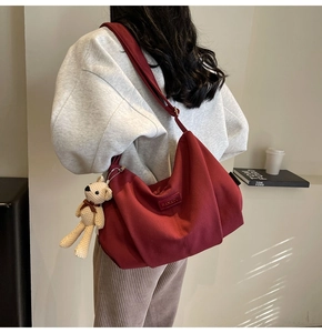 Detail of burgundy nylon crossbody bag with knitted bear charm and leather logo tag