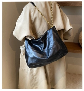 Close-up of black quilted tote bag with gold chain strap on a beige trench coat