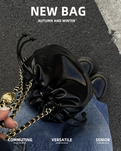 Street style view of a black glossy leather bucket bag with a gold chain strap