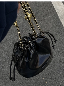 Detail of a black glossy bucket bag featuring gold chain strap and decorative golden ball