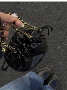 Detail of glossy black drawstring bucket bag with gold chain strap in outdoor setting