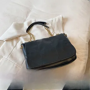 Close-up of black quilted leather shoulder bag with gold chain and triangle stitch texture
