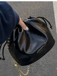 Detail of black drawstring bucket bag with shiny patent texture and gold chain strap
