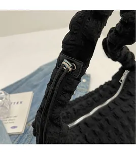Detail of black nylon bubble texture bag featuring wide ruched shoulder strap and silver zip