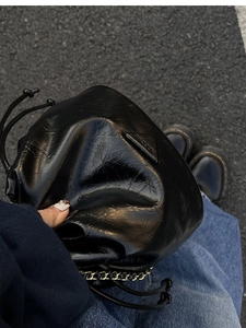 Detail of black drawstring bucket bag featuring pleated faux leather and metal chain strap