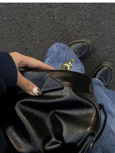 Detail of black pleated bucket bag with metallic logo and gold charm ornament