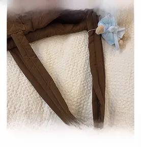 Detail of padded brown nylon handle with quilted pattern and blue bear charm