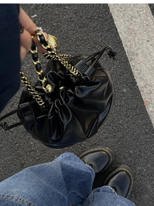 Detail of black glossy leather bucket bag with gold chain strap and metal adjustment ball