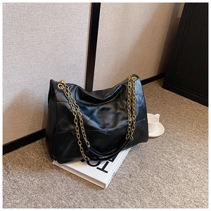 Close-up of black quilted tote bag with large triangle pattern and gold chain straps