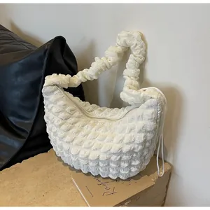 Detailed texture of creamy beige nylon dumpling bag with pleated fabric on stone surface