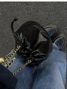Detail of a black cloud-shaped drawstring bucket bag with a gold-tone chain strap