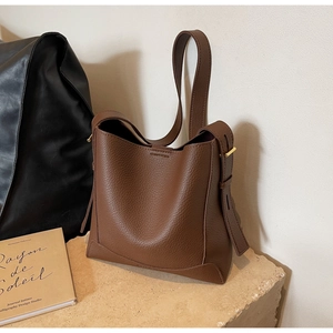 Close-up of brown litchi grain leather bucket bag with gold hardware on a stone base