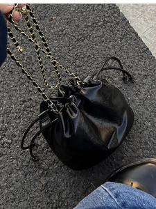 Detail of black glossy drawstring bucket bag featuring a triangle logo and chain strap