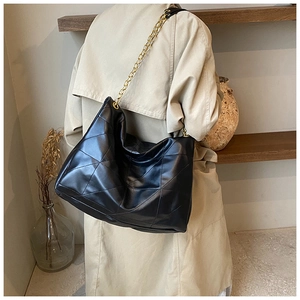 Detailed view of black quilted tote bag with chunky gold chain strap on woman