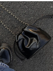 Detail of black glossy pleated bucket bag with gold chain strap and triangle logo