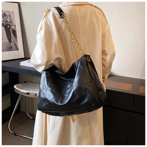 Detail of black quilted leather tote bag with gold chain strap on a trench coat