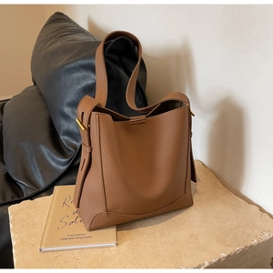 Detail of brown litchi pattern leather bucket bag with gold metal hardware and strap