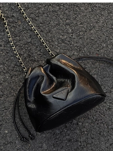Top view of glossy black bucket bag with chain strap on dark pavement texture