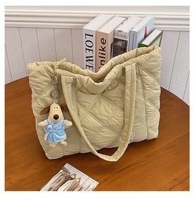 Detail of beige quilted nylon tote bag featuring a cute plush dog charm on dark wood