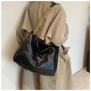 Detailed view of black quilted tote bag with gold chain strap on model shoulder