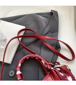 Detail of red leather handbag with heart-patterned silk scarf handle and long strap
