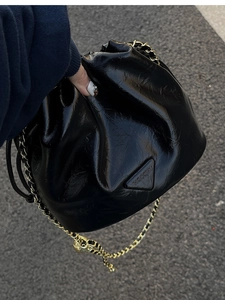 Close-up of a black glossy cloud bag with pleated texture and a gold chain strap
