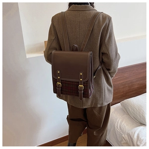 Rear view of a vintage plaid and brown leather backpack worn with a tweed suit