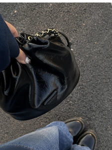 Detail of black glossy pleated bucket bag with gold chain strap and triangle logo plaque
