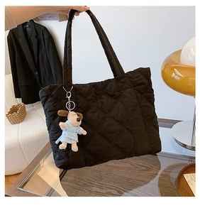 Black quilted nylon tote bag with cute dog plush keychain in a modern home setting