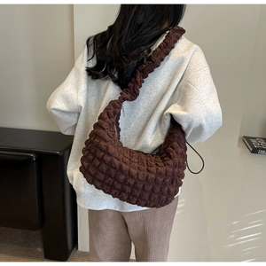 Detail of a brown puffed nylon crossbody bag with stylish ruffle strap shown on model