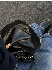 Detailed view of black wrinkled leather shoulder bag with gold chain and metal emblem