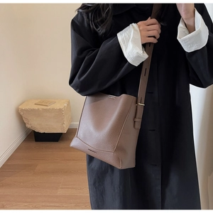 Close-up of brown litchi pattern leather bucket bag with adjustable strap on model