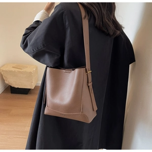 Detail of lychee pattern leather texture and side metal buckle on a dark brown bucket bag
