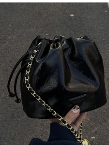 Detail of glossy black drawstring bucket bag with triangular plaque and gold chain strap