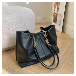 Detail of black pebbled leather tote bag with gold chain strap and side rivet accents