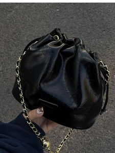 Detail of glossy black pleated bucket bag featuring gold chain and metallic ball charm