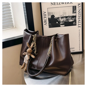 Detailed view of dark brown tote bag featuring gold chain strap and cute rabbit pendant