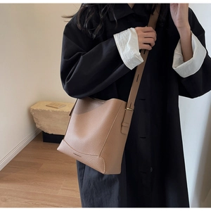 Detail of khaki pebbled leather bucket bag with brand logo and gold hardware strap