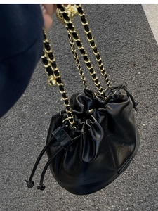 Close-up of black oil wax leather bucket bag with gold chain strap and drawstring detail
