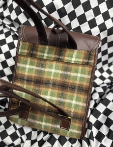 Detail view of the vintage plaid backpack featuring brown leather straps and white stitching