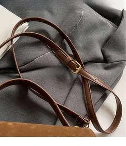 Detail of adjustable brown leather shoulder strap with gold buckle on a crossbody bag