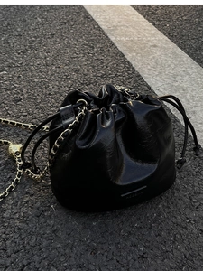 Detail of black drawstring bucket bag with shiny wrinkled texture and gold chain strap