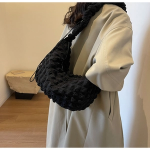 Close-up of black bubble textured nylon shoulder bag on model wearing a beige coat